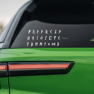 May include: A green car with a white vinyl sticker on the back window. The sticker features a grid of white runes, which are ancient symbols used in Germanic languages.