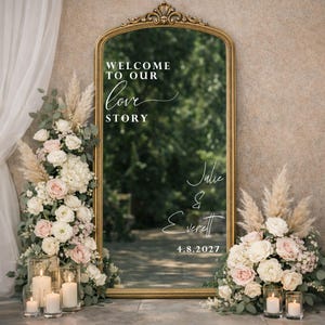 Può includere: Uno specchio da terra ad arco con cornice dorata che riporta il testo bianco "WELCOME TO OUR love STORY" e "Julie & Everett 4.8.2027". Lo specchio è decorato con composizioni di rose bianche e rosa, erba della pampa e portacandele in vetro.