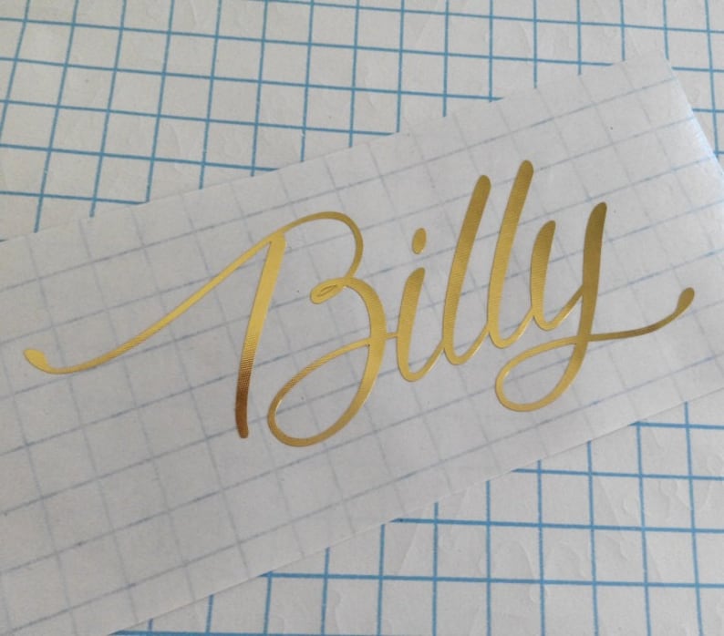 Op de afbeelding: Gouden vinyl sticker met de naam "Billy" in een cursief schrift.