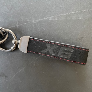May include: Black leather keychain with red stitching and the word "XE" embossed in silver.