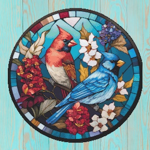 May include: A round stained glass design featuring two birds, a red cardinal and a blue jay, surrounded by white and red flowers and foliage. The birds are perched on a branch against a blue background, framed by a black border.