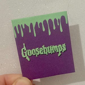 K&ouml;nnte beinhalten: Ein lila und gr&uuml;ner Aufkleber im Goosebumps-Design. Der obere Teil des Aufklebers ist gr&uuml;n mit einem tropfenden Schleim-Design. Das Wort "Goosebumps" ist in gr&uuml;ner, stilisierter Schrift auf dem lila Hintergrund geschrieben.