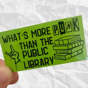 May include: A green sticker with black text and graphics. The text reads "WHAT'S MORE PUNK THAN THE PUBLIC LIBRARY" with a hand gesture and a stack of books. The sticker is rectangular.
