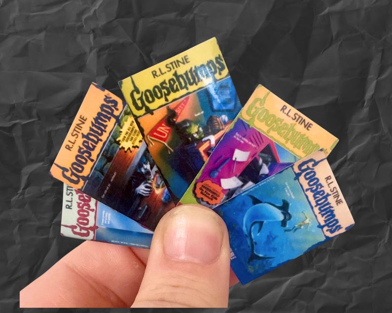 K&ouml;nnte beinhalten: Eine Hand h&auml;lt einen F&auml;cher aus Miniatur-Goosebumps-B&uuml;chern. Die Buchcover zeigen Illustrationen in verschiedenen Farben, darunter Orange, Blau und Gr&uuml;n, wobei der Serientitel deutlich sichtbar ist. Die B&uuml;cher stammen aus der R.L. Stine-Reihe.