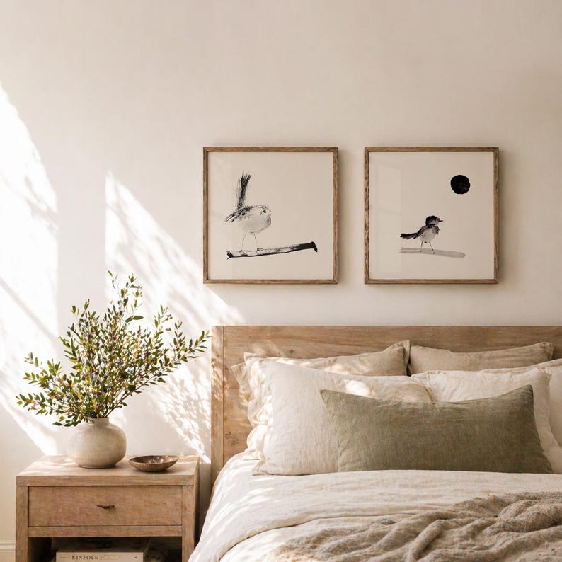 May include: Two square framed wall art prints featuring black ink illustrations of small birds on a light background. The left print shows a bird perched on a branch, while the right print depicts a bird standing below a solid black circle.
