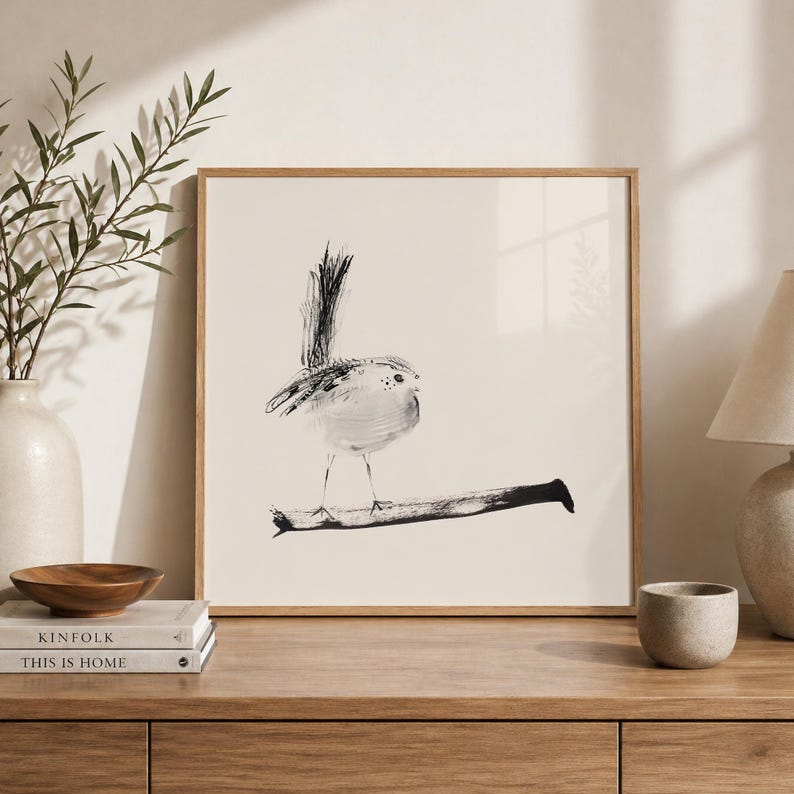 May include: A square framed wall art print featuring a minimalist black ink illustration of a small bird perched on a horizontal branch. The artwork is set against a solid off-white background, showcasing expressive brushstrokes and fine details.