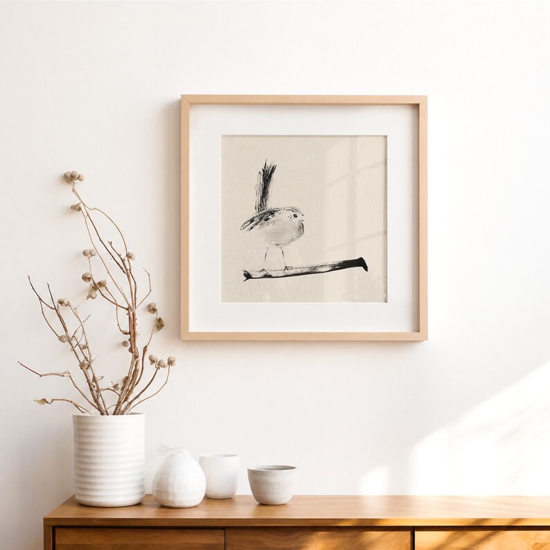 May include: A square framed wall art piece featuring a black and white ink wash illustration of a small bird perched on a thin branch. The artwork is set against a light beige background and enclosed in a simple, light-toned wooden frame.