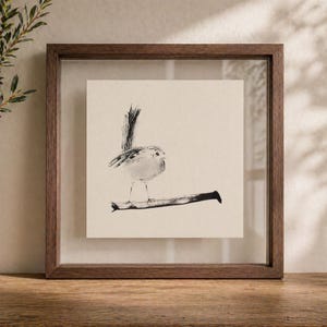 May include: A square framed wall art piece featuring a black ink illustration of a small bird perched on a branch. The artwork is set against a cream-colored background and enclosed within a dark brown wooden frame with a clear glass front.