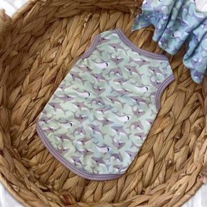 May include: A dog tank top with a shark pattern in shades of gray and white on a light green background. The tank top has a gray trim and is made of a lightweight material. A matching bow is also visible.