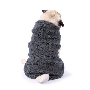 Pode incluir: Um pug vestindo um su&eacute;ter de l&atilde; cinza com capuz para c&atilde;es. O c&atilde;o est&aacute; sentado e olhando para tr&aacute;s por cima do ombro.