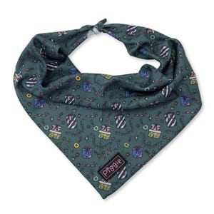 May include: A dark teal dog bandana with a festive Christmas pattern. The bandana features illustrations of wrapped gifts, candy canes, and Christmas lights. The bandana has a knotted top and a small rectangular label with the word "piggies" on it.