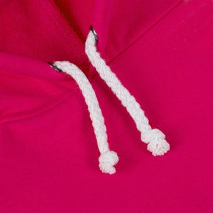 May include: Close-up of a pink hoodie with white drawstring cords. The cords are tied in knots at the ends.