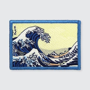 May include: An embroidered patch featuring a blue and white wave, inspired by the famous Japanese woodblock print "The Great Wave off Kanagawa" by Katsushika Hokusai. The patch has a yellow background and a blue border.