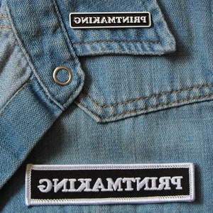 May include: A black and white patch with the word "ЯИКЯМТИИЯ" in white letters on a black background. The patch is sewn onto a blue denim jacket.