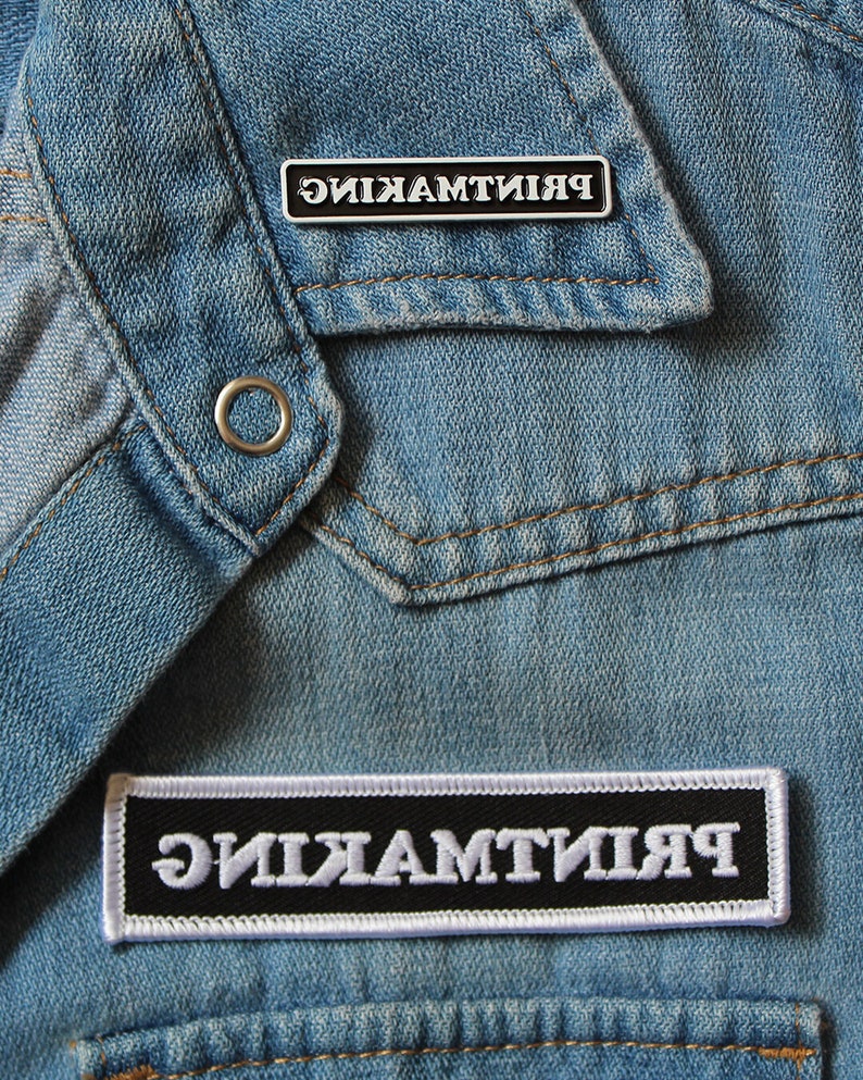 May include: A black and white patch with the word "ЯИКЯМТИИЯ" in white letters on a black background. The patch is sewn onto a blue denim jacket.