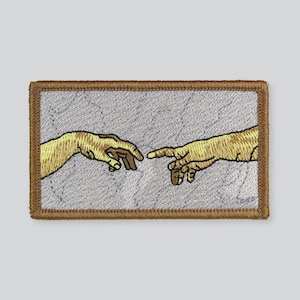 May include: A rectangular embroidered patch featuring a light gray background with a subtle quilted texture. The design depicts two yellow hands reaching toward each other with fingers nearly touching, framed by a thick, solid brown stitched border.