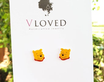May include: A pair of Winnie the Pooh stud earrings. The earrings are made of yellow polymer clay and feature a cartoon image of Winnie the Pooh's face. The earrings are a fun and whimsical way to show your love for the beloved Disney character.