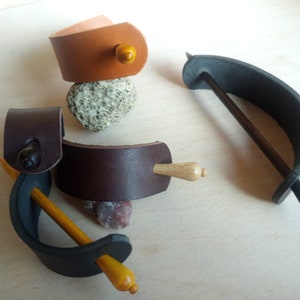 May include: Four leather hair sticks with wooden dowels. Two are brown leather with a dark brown dowel, one is black leather with a light brown dowel, and one is brown leather with a light brown dowel.