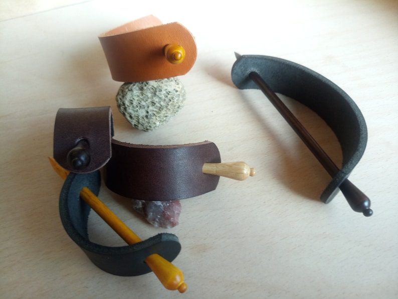 May include: Four leather hair sticks with wooden dowels. Two are brown leather with a dark brown dowel, one is black leather with a light brown dowel, and one is brown leather with a light brown dowel.