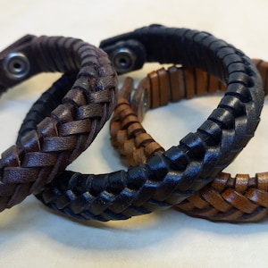 Puede incluir: Tres pulseras de cuero trenzado en marr&oacute;n, negro y marr&oacute;n claro. Las pulseras est&aacute;n entrelazadas y tienen un cierre met&aacute;lico sencillo.