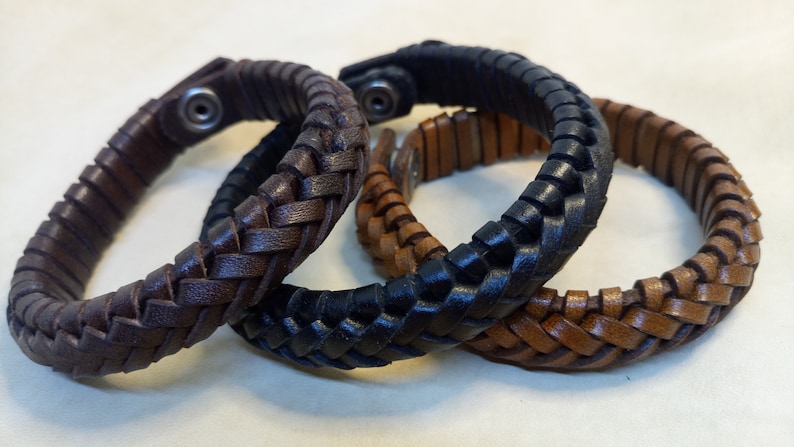 Puede incluir: Tres pulseras de cuero trenzado en marr&oacute;n, negro y marr&oacute;n claro. Las pulseras est&aacute;n entrelazadas y tienen un cierre met&aacute;lico sencillo.