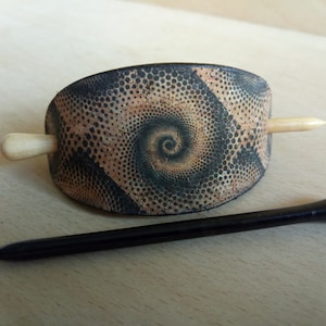 Op de afbeelding: Een bruine en zwarte haarstick met een spiraalpatroon. De stick is gemaakt van kurk en heeft een houten pin.