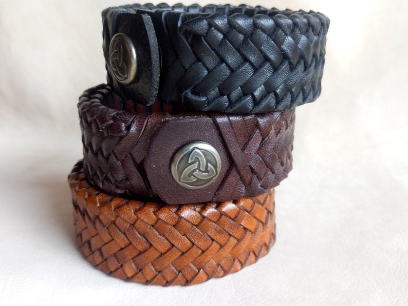 K&ouml;nnte beinhalten: Drei geflochtene Lederarmb&auml;nder mit Metallakzenten. Das obere Armband ist schwarz, das mittlere Armband ist braun und das untere Armband ist beige.
