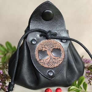 May include: Black leather pouch with a drawstring closure and a brown leather tree of life design. The pouch is decorated with metal rivets.