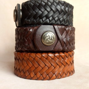 K&ouml;nnte beinhalten: Drei Lederarmb&auml;nder, die &uuml;bereinander gestapelt sind. Das obere Armband ist schwarz, das mittlere Armband ist braun und das untere Armband ist hellbraun. Das mittlere Armband hat einen silbernen Metallverschluss mit einem keltischen Knotendesign.