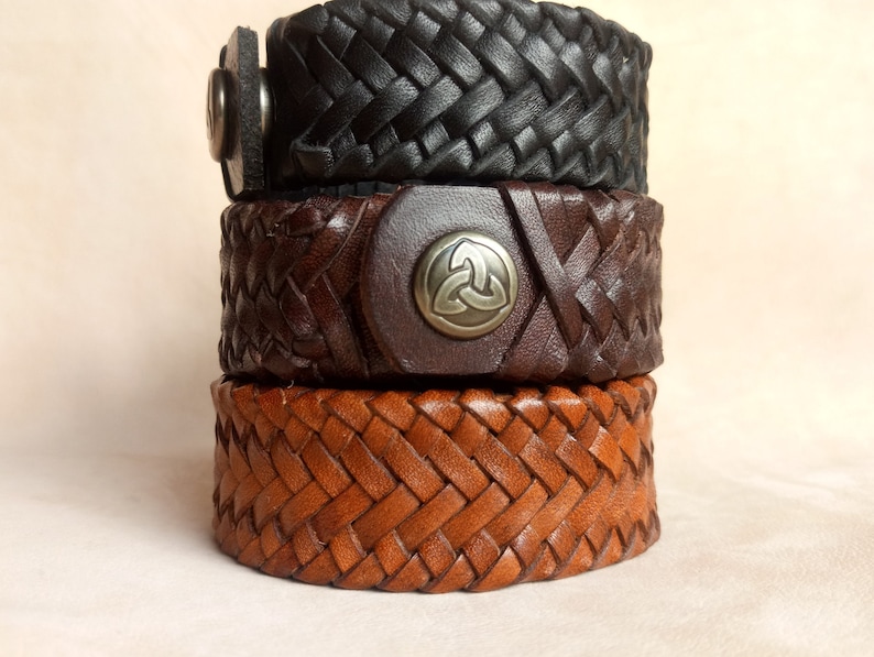 K&ouml;nnte beinhalten: Drei Lederarmb&auml;nder, die &uuml;bereinander gestapelt sind. Das obere Armband ist schwarz, das mittlere Armband ist braun und das untere Armband ist hellbraun. Das mittlere Armband hat einen silbernen Metallverschluss mit einem keltischen Knotendesign.