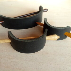 May include: Two black leather hair clips with wooden hair sticks. One hair stick is brown and the other is light wood.