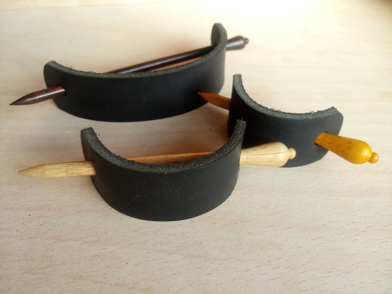 May include: Two black leather hair clips with wooden hair sticks. One hair stick is brown and the other is light wood.