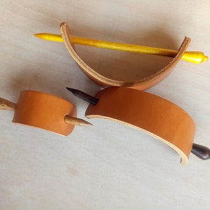 May include: Three leather hair clips with wooden dowels. The clips are brown leather and the dowels are natural wood, black, and yellow.