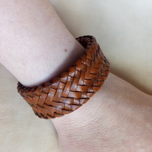 K&ouml;nnte beinhalten: Ein braunes Lederarmband mit geflochtenem Muster.