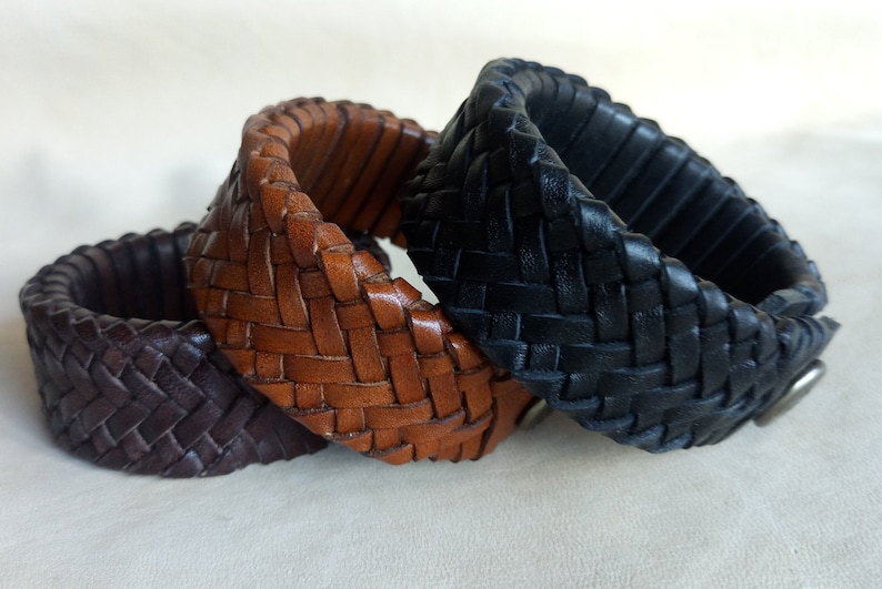 K&ouml;nnte beinhalten: Drei Lederarmb&auml;nder in Braun, Schwarz und Dunkelbraun, geflochten in einem Fischgr&auml;tenmuster.
