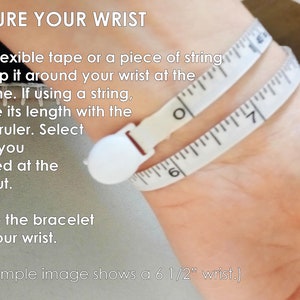 K&ouml;nnte beinhalten: Nahaufnahme einer Hand mit einem Ma&szlig;band, das um das Handgelenk gewickelt ist. Der Text lautet "MEASURE YOUR WRIST" und enth&auml;lt Anweisungen, wie man sein Handgelenk f&uuml;r ein Armband misst. Der Text lautet auch "(This example image shows a 6 1/2" wrist.)"