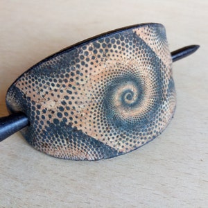 Op de afbeelding: Een zwarte en bruine haarstick met een spiraalpatroon. De stick is gemaakt van kurk en heeft een zwarte houten pin.