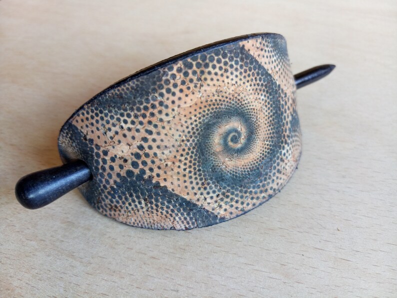 Op de afbeelding: Een zwarte en bruine haarstick met een spiraalpatroon. De stick is gemaakt van kurk en heeft een zwarte houten pin.