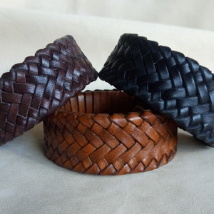 K&ouml;nnte beinhalten: Drei geflochtene Lederarmb&auml;nder in Braun, Dunkelbraun und Schwarz. Die Armb&auml;nder sind mit einem einfachen Muster gewebt und haben eine glatte, polierte Oberfl&auml;che.