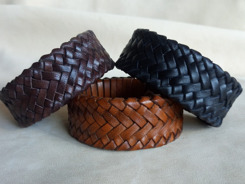 K&ouml;nnte beinhalten: Drei geflochtene Lederarmb&auml;nder in Braun, Dunkelbraun und Schwarz. Die Armb&auml;nder sind mit einem einfachen Muster gewebt und haben eine glatte, polierte Oberfl&auml;che.