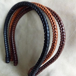 May include: Four braided leather headbands in black, brown and tan. The headbands are curved and appear to be made of high-quality leather. The headbands are likely for fashion or hair accessories.