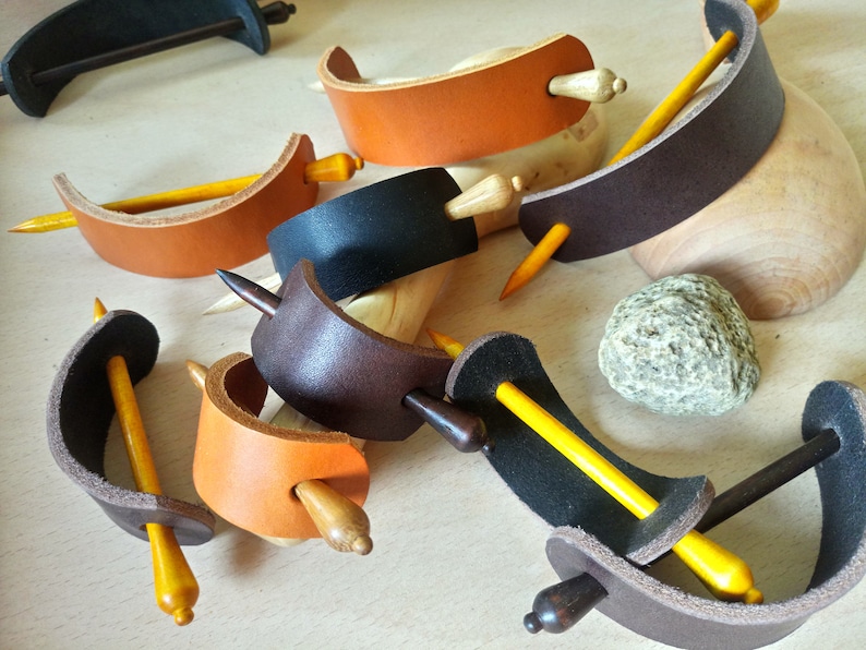 May include: Assortment of leather hair clips with wooden dowels. The clips are in various colors, including brown, black, and orange. The dowels are all yellow.