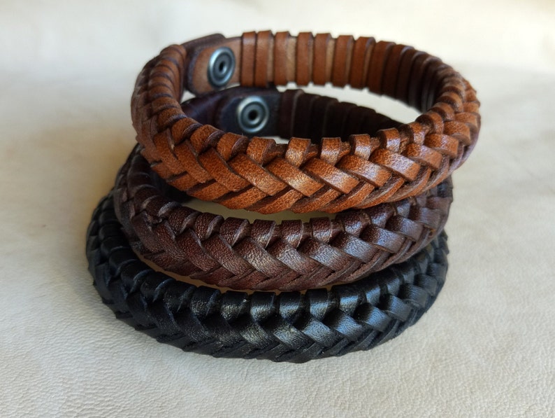 Puede incluir: Tres pulseras de cuero trenzado en marr&oacute;n, marr&oacute;n oscuro y negro. Las pulseras est&aacute;n apiladas una encima de la otra.