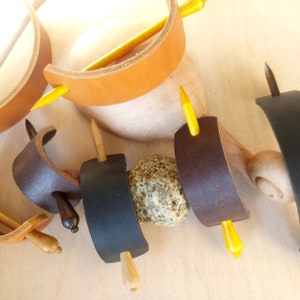 May include: Assortment of leather hair stick holders in brown, black, and dark brown with wooden hair sticks. Some sticks are yellow, brown, and dark brown.