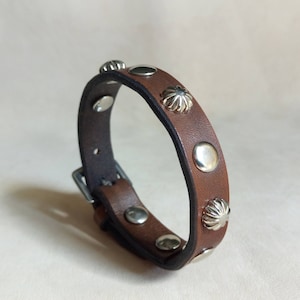 Peut inclure: Un bracelet en cuir marron avec des clous argentés. Le bracelet a une fermeture à boucle.