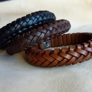 Puede incluir: Tres pulseras de cuero trenzado en negro, marr&oacute;n y marr&oacute;n claro. Las pulseras est&aacute;n apiladas una encima de la otra.
