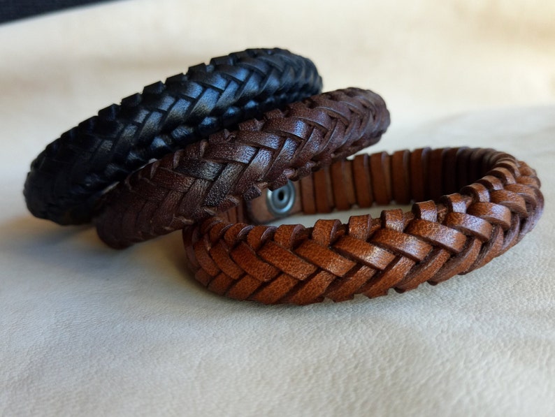 Puede incluir: Tres pulseras de cuero trenzado en negro, marr&oacute;n y marr&oacute;n claro. Las pulseras est&aacute;n apiladas una encima de la otra.