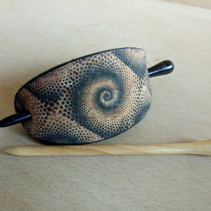 Op de afbeelding: Een zwarte en bruine haarstick met een spiraalpatroon. De stick is gemaakt van hout en heeft een zwarte handgreep.