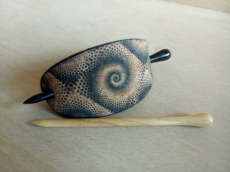 Op de afbeelding: Een zwarte en bruine haarstick met een spiraalpatroon. De stick is gemaakt van hout en heeft een zwarte handgreep.