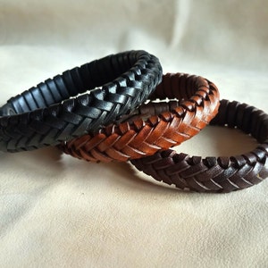 Puede incluir: Tres pulseras de cuero trenzado en negro, marr&oacute;n y beige. Las pulseras est&aacute;n apiladas una encima de la otra.